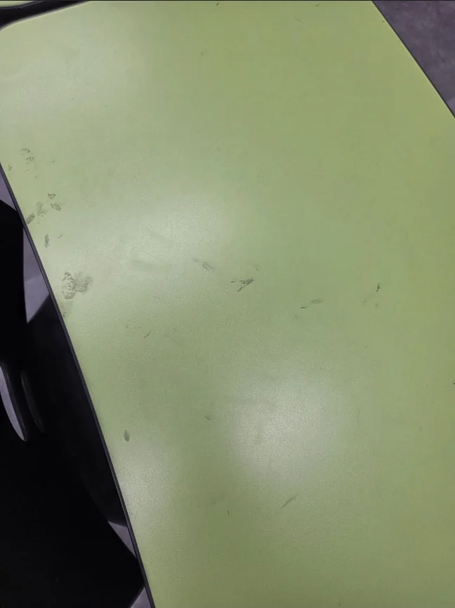 학원 책상 상판의 작은 얼룩과 흔적을 가까이서 확인하는 모습